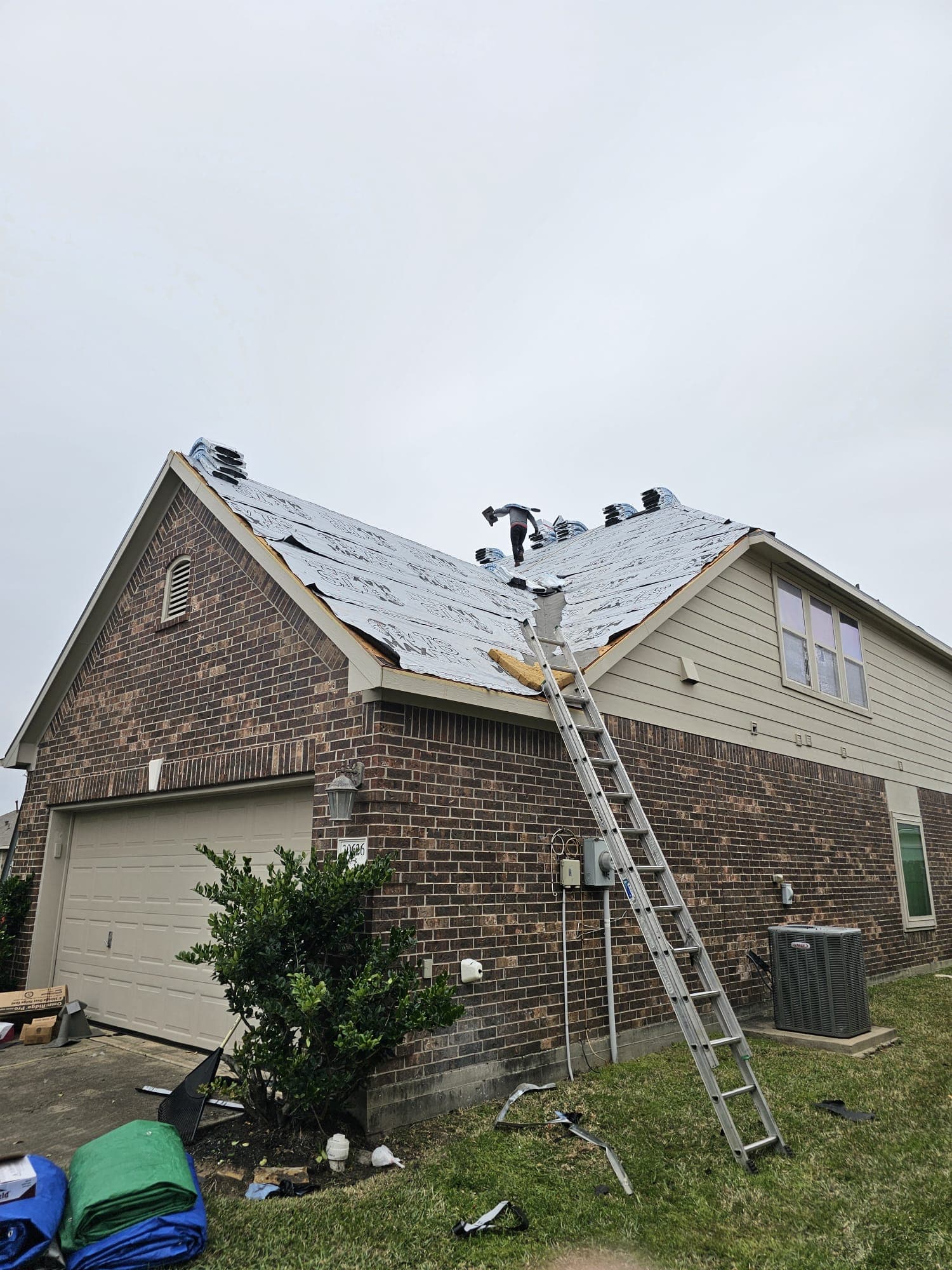 Crew on underlayment with a dumpster trailer staged in the driveway of a two-story brick home