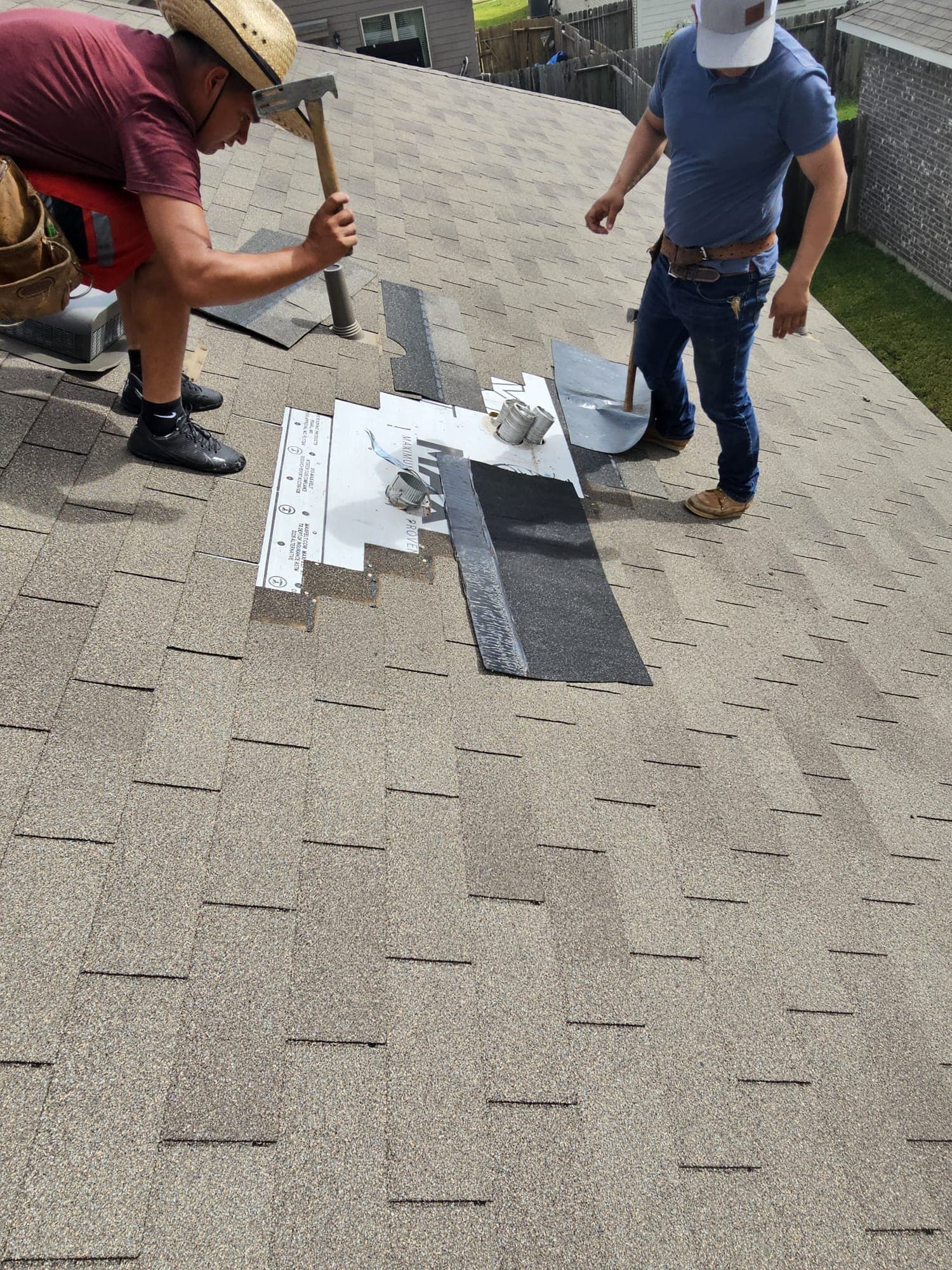 Crew on a roof installing ridge-cap shingles with hammer and nail gun