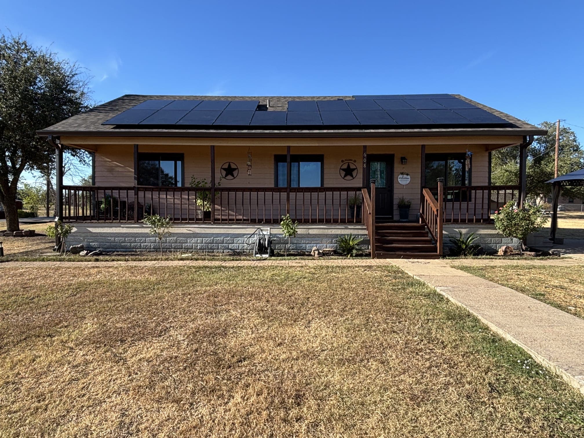 Tan bungalow in Katy, Texas with a full black solar panel array, covered porch and Texas star accents